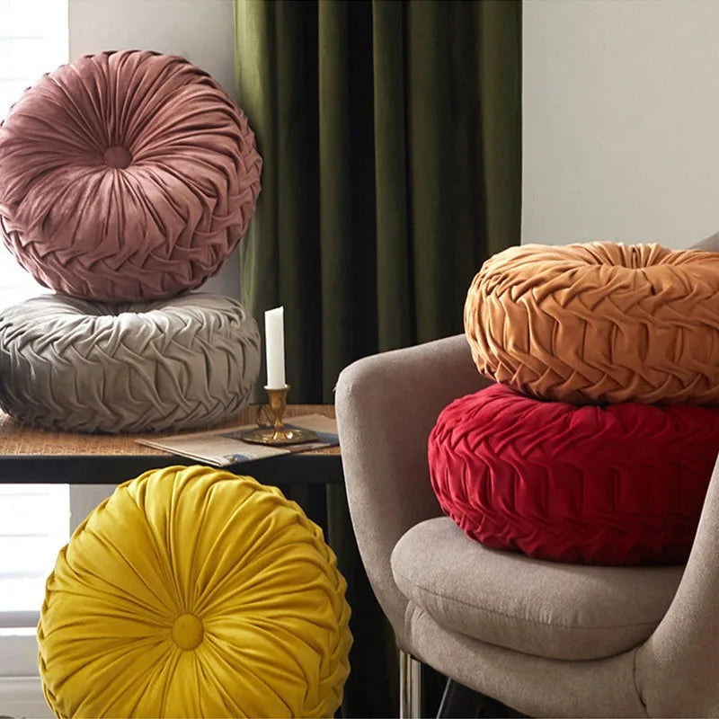 Coussin rond plissé en velours vert, orné d'un bouton central, posé sur un fauteuil beige.