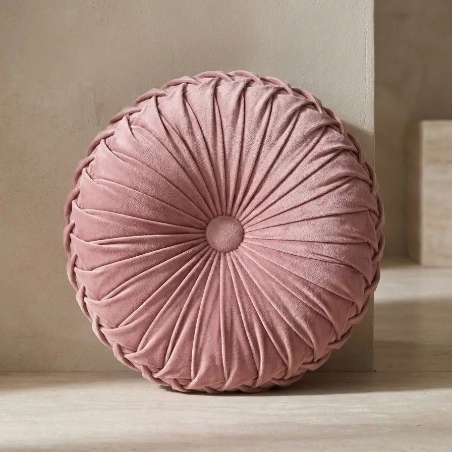 Coussin rond plissé en velours rose.